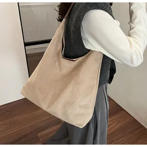 Detailed close-up of a large beige suede tote bag worn as a stylish underarm shoulder bag