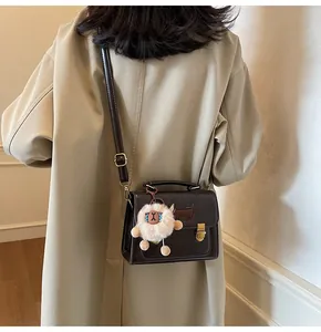 Detail view of a dark brown crossbody bag with a white plush sheep charm and long strap