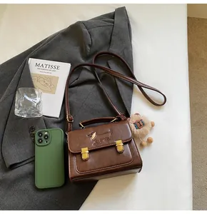 Detail of vintage brown leather square bag with dog pattern and plush pendant on a bed