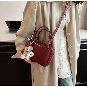 Dunkelrote Handtasche mit glänzendem Finish und süßem Plüschbär-Anhänger Detail