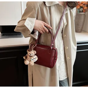 Detail einer burgunderroten Lederhandtasche mit Bärenanhänger in einer Büroumgebung