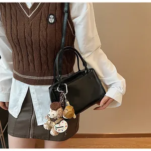Details einer schwarzen Glanztasche mit Plüschbär-Anhänger und Paletten-Accessoire
