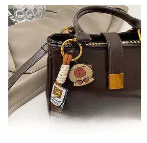 Detail of Capybara bag charm with woven lanyard on a vintage brown leather handbag