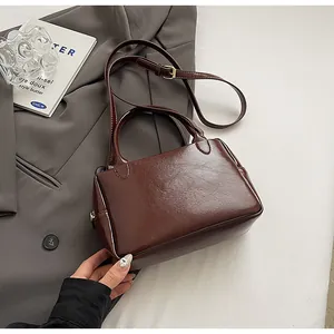 Detail einer tiefbraunen Lederhandtasche auf einem Blazer, Textur und Griff zeigend