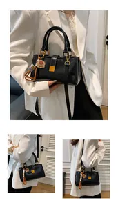 Detail view of glossy black rectangular handbag with gold hardware and cartoon charm