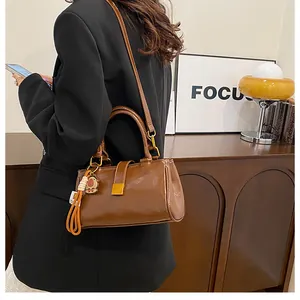 Detail view of brown leather handbag featuring golden buckles and cartoon charm accessories