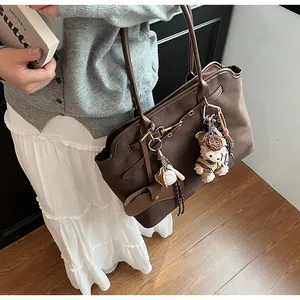 Detail view of large dark brown suede tote bag with teddy bear charm and gold hardware