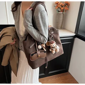 Detail of dark brown matte suede tote bag featuring small bear pendant and card holder accessory