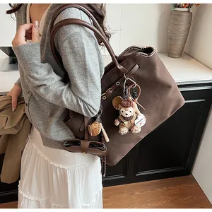Close-up of brown frosted suede tote bag with decorative plush charms and side drawstrings