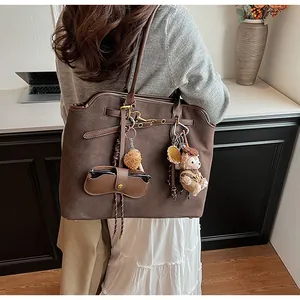 Detail of a large brown suede tote bag featuring a cute teddy bear charm and accessories