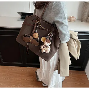 Macro detail of brown frosted suede tote bag with plush bear and vintage charms
