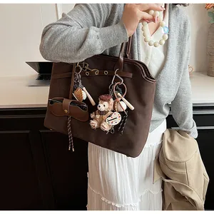 Detail of a brown suede tote bag with leather straps and decorative plush pendants