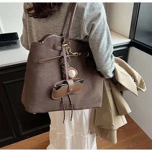 Detail of large brown faux suede tote bag with baseball charm on shoulder of a model