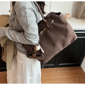 Close-up of a large brown suede tote bag with leather handles on a model in a minimal setting