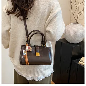 Detail of dark brown glossy leather handbag featuring dual handles and gold square buckle