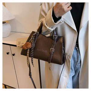 Detail view of coffee brown leather tote bag with strap buckle and plush toy charm
