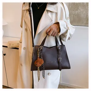 Detail of dark brown leather tote bag with embossed logo and plush bear charm accessory