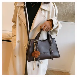 Detail of a deep brown leather tote bag with logo embossing and a cute plush bear charm