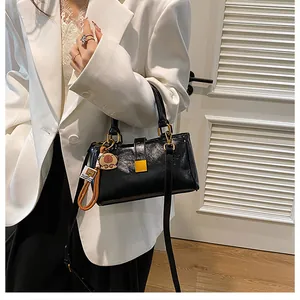 Detail of black glossy square handbag with gold buckle and a cute bear charm accessory