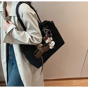 Detail of a large black suede tote bag with plush Duffy pendant and leather accessories