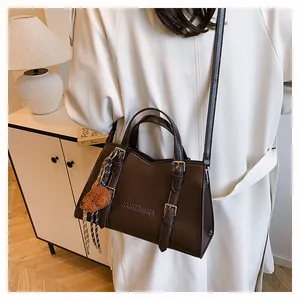 Close-up of dark brown PU leather tote bag with logo, metal buckle and plush charm