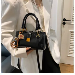 Detail of a shiny black PU leather crossbody bag with gold buckle and cute doll pendant