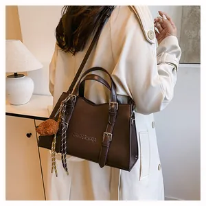 Detail of dark brown tote bag featuring reinforced handles and a cute plush animal charm
