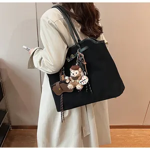 Detail of black suede tote bag with cute teddy bear charm and colorful tag accessory