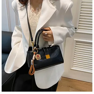Detail of black crossbody bag with gold buckle and a cute bear charm on white suit