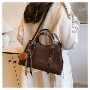Detail of dark brown tote bag with embossed lettering and plush animal charm