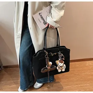 Close-up of black suede tote bag with a decorative plush bear and leather charm details