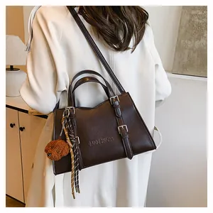 Detail of dark brown leather tote bag with teddy bear charm and braided tassel decor