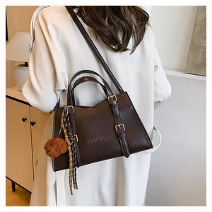 Detail of deep brown tote bag featuring textured leather, embossed logo, and a cute bear charm