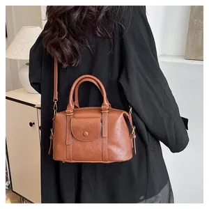 Borsa Boston vintage marrone con finiture dorate indossata a tracolla su un cappotto nero