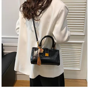 Detail view of black glossy shoulder bag featuring golden square lock and cute bear charm