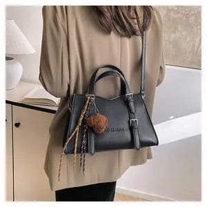 Detail of black leather tote bag featuring brand logo, metal buckles and plush bear charm