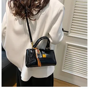 Close-up of black patent leather crossbody bag with gold buckle and bear tassel detail