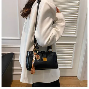 Detail of a black rectangular shoulder bag with gold square buckle and a cute bear charm