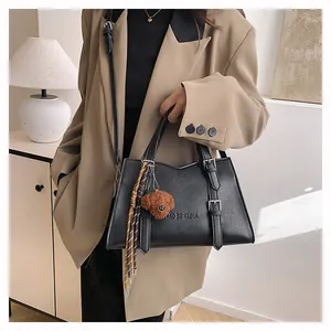 Detail of matte black tote bag with metal buckles, logo embossing and teddy bear charm