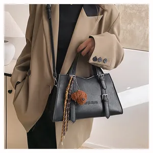 Detail of black pebbled leather tote bag with teddy bear charm and adjustable strap