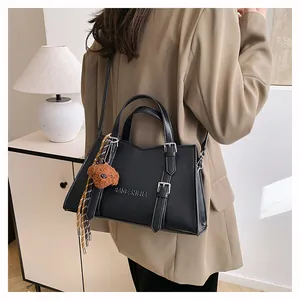 Detail of black leather tote bag with silver buckle and cute brown plush bear charm
