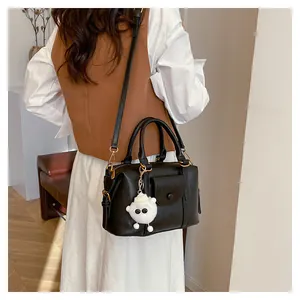 Vista macro di una borsa Boston nera con ciondolo agnello di peluche e cerniera d'oro