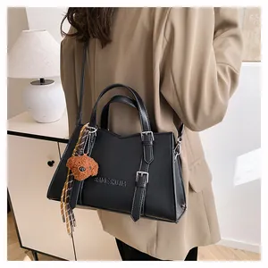 Detail of black leather tote bag featuring a plush bear charm and metallic buckle straps