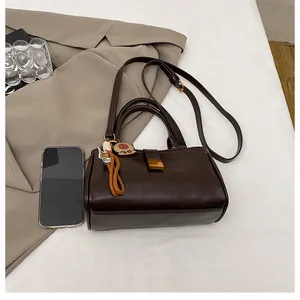 Close-up of brown shiny leather crossbody bag with gold buckle and cute cat charm decoration