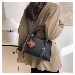 Detail of black leather tote bag with embossed logo, plush bear charm and plaid scarf