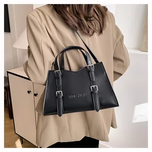 Black leather tote bag with buckle straps worn over a beige blazer by a model