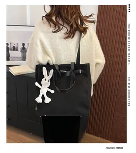 Detail of black canvas tote bag with leather handles and cute rabbit plush charm