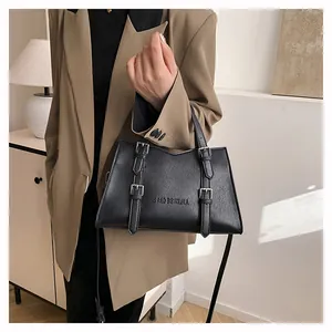 Detail of black textured leather tote with metal buckles and branding on a khaki blazer