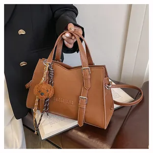 Detail view of large brown faux leather tote bag with brand logo and plush puppy charm