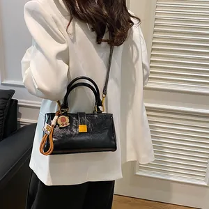 Glossy black leather crossbody bag with gold hardware and bear charm on a model